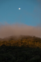 Montanha no p&ocirc;r do sol com n&eacute;voa e lua cheia