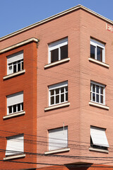 Facade of a red brick residential building with symmetrical windows and white awnings, urban architecture on a clear day