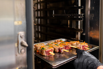 A tray of seasoned raw steaks is being placed into an industrial oven, capturing the concept of food preparation in a professional kitchen. image highlights the culinary process and art of cooking.