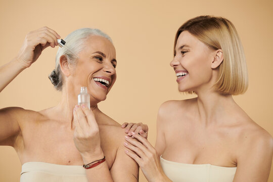 Two women share laughter while applying skincare products together.