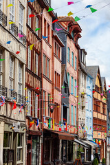 Obraz premium ROUEN, NORMANDY, FRANCE, JUNE 12, 2019: Damiette street, narrow pedestrian cobbled street, antique shop district, flag decoration for Armada tall ship festival, saint Ouen abbey in background