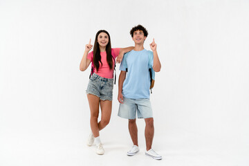 Full length of high school pupils students teenagers classmates boy girl friends in casual with bags looking pointing index finger up isolated on white background. Education advertisement concept