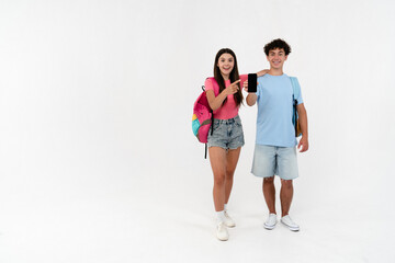 Obraz premium Full length of high school pupils students teenagers classmates boy girl friends with bags holding using smart mobile phone showing mock up screen pointing fingers isolated on white background.