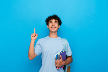 Smiling boy guy high school male pupil student teenager with bag holding books copybooks having idea pointing index finger up isolated on blue background. Education back to school concept