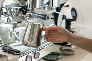 A barista whips milk for cappuccino in a coffee shop. Close-up of the barista's hands.