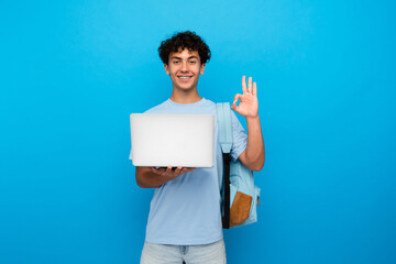 Young teenager high school boy guy holding laptop computer showing okay gesture while using it for...