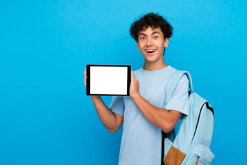 Happy surprised boy guy high school male pupil student teenager with bag holding using digital tablet for e-learning showing demonstrate mock up white empty screen isolated over blue background