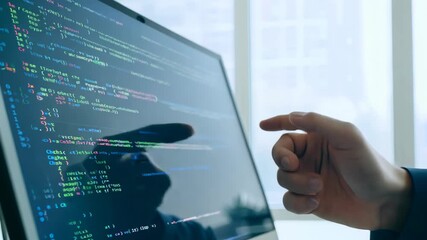 A man in a suit works at a computer with programming code displayed on the screen