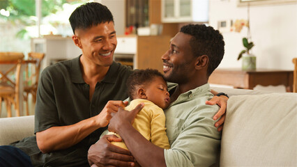 Same Sex Male Couple Smiling While Holding a Sleeping Child in a Bright Living Room