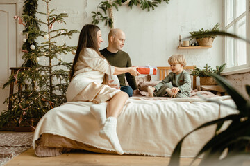Obraz premium Warm and cozy lifestyle photo of happy young family. young family dad mom and little son playing on the bed in Christmas decor.Winter, New Year home decor. christmas home cozy interior