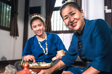 Smiling Thai mother and daughter in indigo clothing  eating Kantok dinner traditional northern Thai...