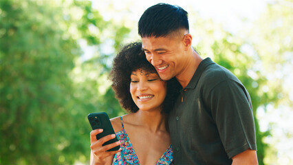 Young Couple Enjoying Time Together While Using a Smartphone in a Park on a Sunny Day