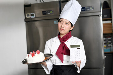 厨房で電卓とケーキを持ち悩む女性料理人