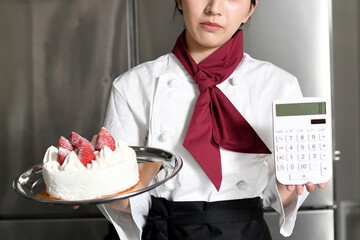 厨房で電卓とケーキを持ち悩む女性料理人