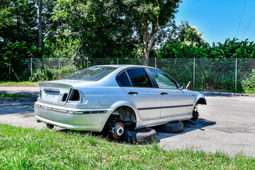 A silver car that has a flat tire is currently sitting in the grass