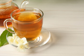 Hot jasmine tea in cup and flowers on white wooden table, space for text
