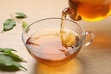 Pouring refreshing green tea into cup at wooden table, closeup