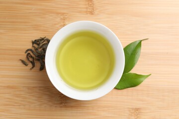 Refreshing green tea in cup and leaves on wooden table, top view