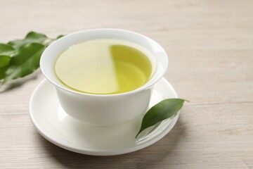 Refreshing green tea in cup and leaves on wooden table, closeup