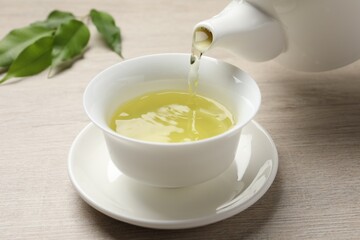 Pouring refreshing green tea into cup at wooden table, closeup