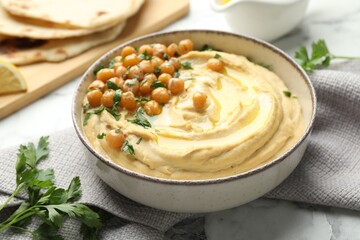 Delicious hummus with olive oil, chickpeas and parsley in bowl on table