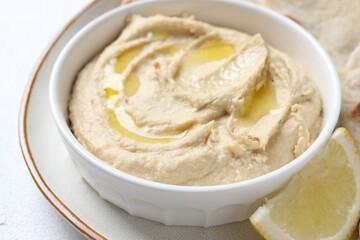 Delicious hummus with olive oil in bowl and lemon on white table, closeup