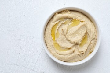 Delicious hummus with olive oil in bowl on white textured table, top view. Space for text