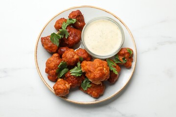Baked cauliflower buffalo wings with parsley and sauce on white marble table, top view