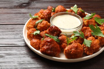 Baked cauliflower buffalo wings with parsley and sauce on wooden table, closeup