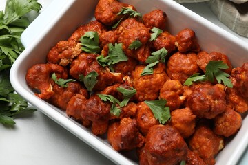 Baked cauliflower buffalo wings in baking dish and parsley on white table, top view