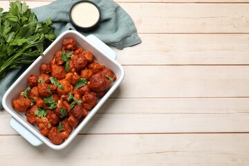 Baked cauliflower buffalo wings in baking dish, sauce and parsley on wooden table, top view. Space for text