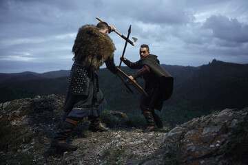 Fierce fight between two medieval barbarian warriors against dramatic landscape