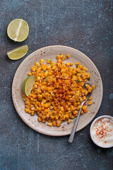 Plate of esquites, a popular mexican street food dish, are served with lime wedges and sour cream with chili powder