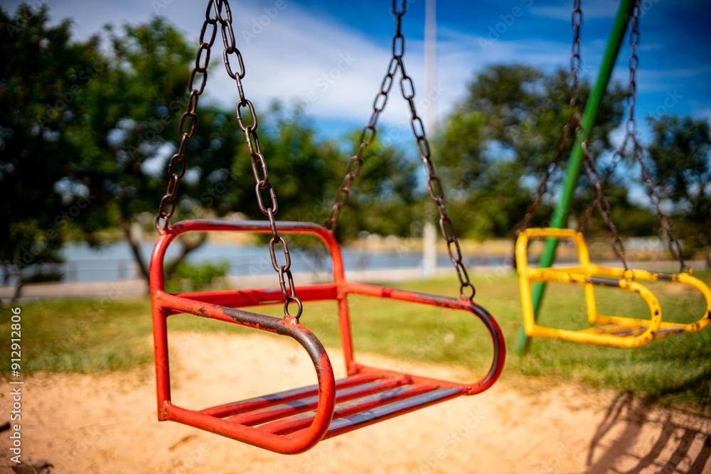 Wall mural red swing in a playground on a sunny day with a blurred background of trees. brazil