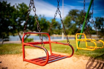 Red swing in a playground on a sunny day with a blurred background of trees. Brazil