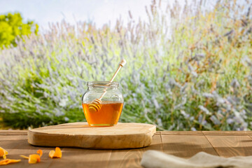 Honey in jar on outdoor wooden table with garden meadow flowers background. 