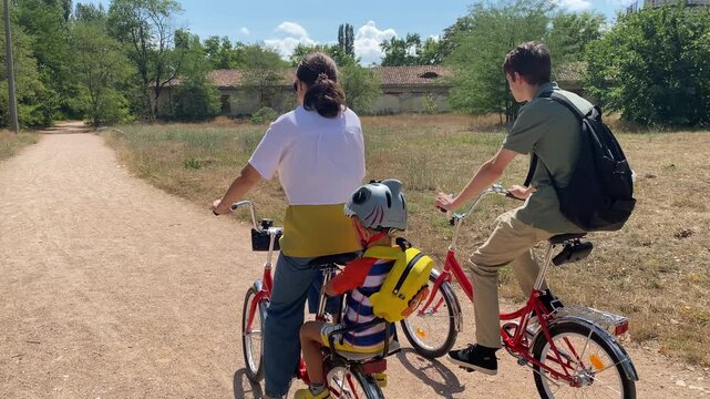 Family bike ride in the park. Mother with two sons riding bicycles on the path in summer. Simferopol, Crimea, Russia 2024