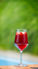 Glass of red iced beverage on a wooden surface with lush green foliage in the background