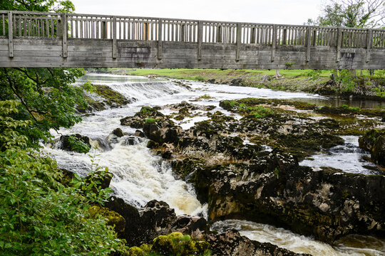Grassington Yorkshire. A rustic wooden bridge over a cascading river surrounded by lush greenery and rocky terrain.