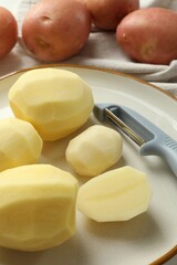 Fresh raw potatoes and peeler on table, closeup