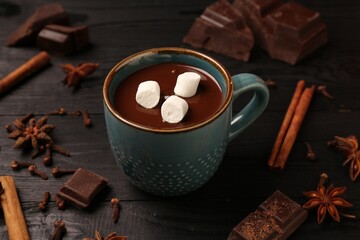 Tasty melted chocolate with marshmallows in cup and spices on dark wooden table, closeup