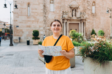 Obraz premium Young beautiful 30s woman looking city map at street, old town. Attractive young female tourist is exploring new city. Traveling Europe, High quality photo