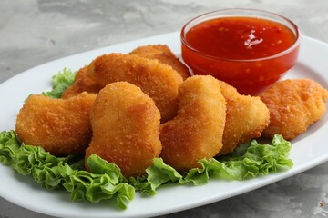 Tasty chicken nuggets with chili sauce and lettuce on grey textured table, closeup