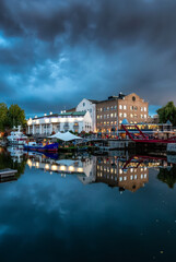 Boats in marina with restaurants and hotels in a modern city. London, United Kingdom. Travel Destination. Night after cloudy sunset.