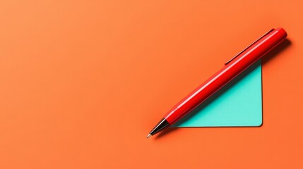 Red pen lying flat on a turquoise notepad, casting natural shadows, with an eye-catching orange background perfect for educational concepts