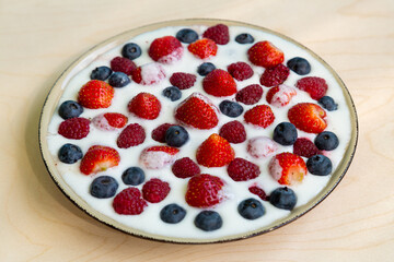 In a plate with whipped cream, strawberries, raspberries and blueberries on a gray table