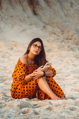 Beautiful brunette girl wearing glasses sitting at the beach using her cell phone