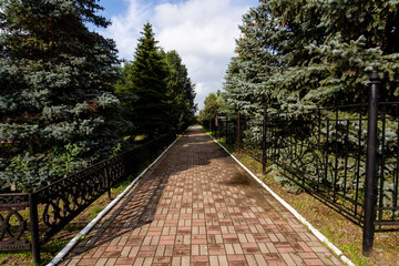 A charming brick walkway is beautifully situated within a park that is surrounded by lush green trees and a protective fence, creating a peaceful, inviting atmosphere for visitors