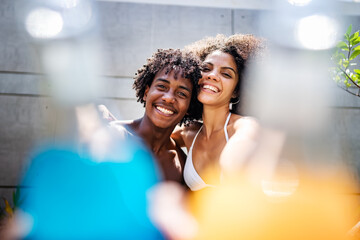 Young couple of African descent enjoying a sunny day at a luxurious pool. They are sitting at the...