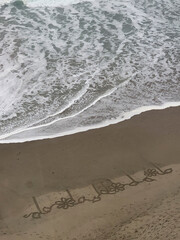 Cryptic message written in the sand, bird's eye view as waves come in about to erase the message.